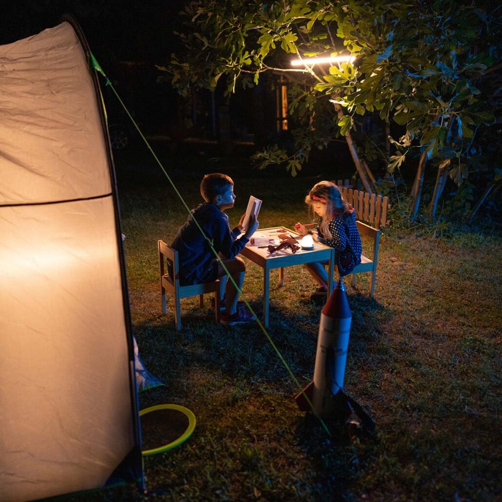 Naturkinder: draussen schlafen (Kinder sitzen im Dunkeln vor einem Zelt